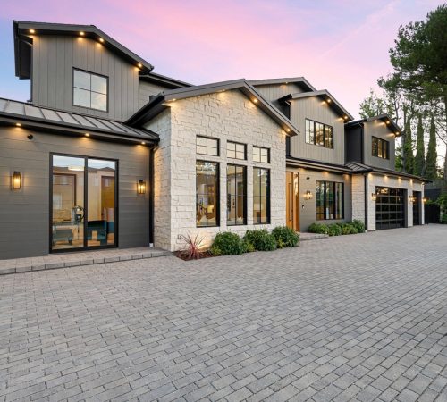 Modern luxury home exterior with a spacious driveway and well-lit facade at sunset.
